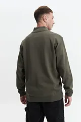 Sweater verde oliva de punto con cuello alto y cierre de medio cierre. Tiene puños y logo bordado en el pecho.