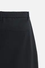Pantalón negro de corte slim fit, confeccionado en tejido elástico. Cuenta con cintura elástica, bolsillos frontales y traseros de vivo. Cierre frontal con cremallera y botón.
