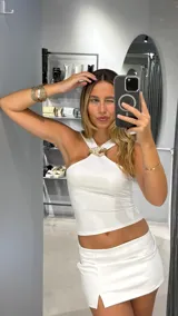 Top blanco con cuello halter y detalle de aplique dorado en el centro.