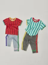 Pantalón de jean celeste con efecto lavado, corte recto y largo a la rodilla. Presenta una cinta vertical color violeta en la pierna izquierda, una cinta vertical color verde en la pierna derecha y una cinta horizontal color rosa en la parte inferior de ambas piernas.