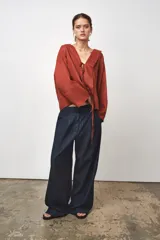 Blusa color ladrillo confeccionada en lino 100%. Tiene cuello fluido, mangas largas acampanadas y espalda descubierta ajustable con cordones.