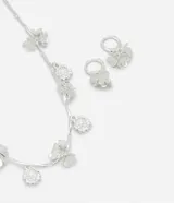 Conjunto de collar y caravanas plateados con colgantes de flores con incrustaciones de strass. El collar es de cadena fina con colgantes de flores espaciados. Las caravanas son aros pequeños con un dije de flor colgando.