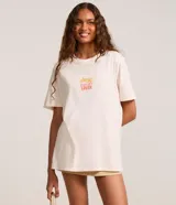 Remera alargada de algodón color crema con estampa de palmeras y atardecer en la playa.