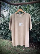 Remera oversize de manga corta, color beige lavado, con estampado circular en la espalda que incluye una palmera y texto que dice "SUNSET", "PALM", "TROPICAL" y "BEACH TRIP".