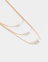 Collar corto de triple cadena dorada con perlas blancas de diferentes tamaños.