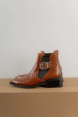 Botines Chelsea color beige con elásticos laterales negros, punta cuadrada, detalle de hebilla lateral y tacón bloque bajo.