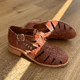 Sandalias franciscanas de cuero color marrón con tiras entretejidas, hebilla lateral y taco bajo de madera.