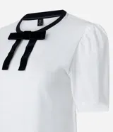 Blusa blanca de media malla de algodón, con cuello redondo con ribete negro y moña de terciopelo negra. Tiene mangas cortas abullonadas.