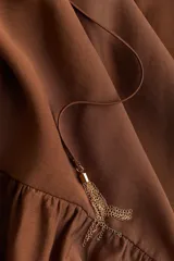 Vestido largo marrón con escote cuadrado y cordón ajustable con borlas. Mangas cortas abullonadas con forro y ribete elástico oculto.