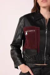 Campera corta de cuero sintético negra con detalles en gamuza color borgoña en la parte superior del pecho y bolsillos con cierre.