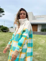 Buzo largo con cuello alto de polar color crema y cuerpo con estampado de cuadros en tonos celeste, amarillo y blanco.