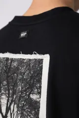 Remera color crudo, corte oversize, mangas cortas y cuello redondo. Estampado frontal con dos árboles unidos por sus raíces y parche estampado en la espalda con una silueta de mano que se fusiona con ramas.