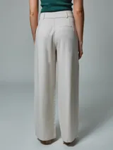 Pantalón de vestir color crudo, de corte recto, con bolsillos laterales y traseros. Se ajusta a la cintura con cinturón de cuero marrón.