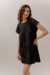 Vestido corto negro con diseño tejido en bloques y detalles dorados, de corte recto y mangas cortas. Confeccionado en Uruguay con 50% poliéster y 50% algodón.