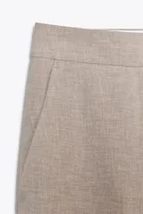 Pantalón de vestir color beige, de tiro bajo, corte recto y largo cropped. Cuenta con bolsillos laterales y traseros, cierre frontal con cremallera y gancho metálico, y abertura lateral en el bajo.