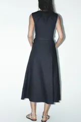 Vestido midi de denim azul oscuro, sin mangas, con cuello redondo, bolsillos laterales, cinturón con hebilla metálica y cierre frontal con cremallera.