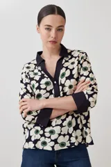 Blusa con estampa de margaritas blancas y verdes sobre fondo azul marino, con cuello polo y mangas 3/4 con puños en contraste.