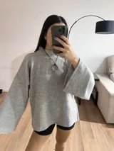 Sweater gris de tejido de punto grueso, con cuello alto, mangas anchas y aberturas laterales.