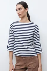 Buzo de cuello redondo con estampado de rayas horizontales blancas y azul marino. Presenta mangas de largo 3/4 con un panel lateral en contraste, botones decorativos y terminación en volados.