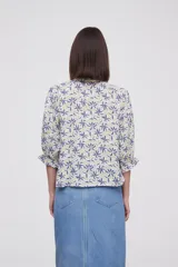 Blusa estampada con flores azules y hojas verdes, cuello mao con volados, mangas 3/4 con volados en los puños y cierre frontal con botones.