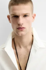 Camisa de algodón color blanco hueso, de corte relajado (relaxed fit), con cuello solapa y manga larga terminada en puño con botón. Cierre frontal con botonadura.