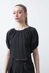 Top negro de manga corta con escote redondo y frunces en la costura de la sisa, creando un efecto de manga abullonada. El tejido parece ligero y con textura.