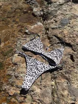 Conjunto de bikini blanco con estampado de manchas negras. El corpiño es de triángulo fijo con tirantes finos y la bombacha es tipo less regulable.