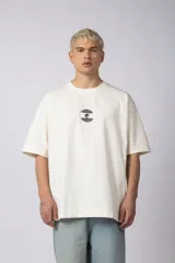 Remera color crudo, corte oversize, mangas cortas y cuello redondo. Estampado frontal con dos árboles unidos por sus raíces y parche estampado en la espalda con una silueta de mano que se fusiona con ramas.