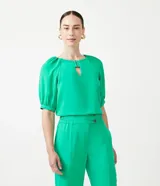 Blusa verde de crepé con cuello redondo, manga corta abullonada y abertura en forma de gota en el escote.