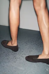 Zapato mocasín de mujer color marrón oscuro, confeccionado en serraje con detalle de tira en la parte delantera y acabado en punta redonda.