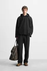 Sudadera con capucha negra, de corte oversize, confeccionada en tejido de algodón con interior en rizo. Cuenta con manga larga, bolsillos frontales tipo canguro, efecto lavado y acabados irregulares con vuelta.