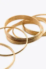 Pack de siete pulseras rígidas metálicas doradas con textura acanalada.