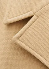 Abrigo corto color beige, de corte recto y doble botonadura. Tiene cuello con solapa, bolsillos laterales y mangas largas con puños abotonados.