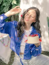 Camisa crop azul con estampado de motivos de fiesta, cuello camisero, mangas largas con puños abotonados y lazos para atar en la cintura.