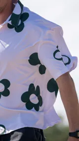 Camisa de manga corta, color blanco, con estampado de flores grandes en verde oscuro. Tiene cuello camisero y cierre frontal de botones.
