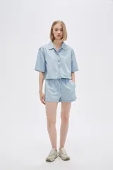 Camisa celeste de jean, corte cropped, con cuello camisero, cierre frontal con botones y mangas cortas.