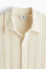 Camisa color crudo de punto pointelle con estilo crochet, de manga corta, cuello inglés, botones frontales y bajo recto.