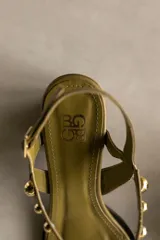 Sandalia de cuero color marrón con taco bloque medio y punta cuadrada. Presenta tachas esféricas doradas en las tiras y hebilla de ajuste en el tobillo.