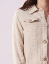 Campera color beige de algodón con cuello camisero, abertura central con botones de madera, bolsillos de parche en el pecho y mangas largas con puños abotonados.