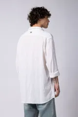 Camisa blanca de lino con cuello clásico, manga larga con puños abotonados y corte holgado. 