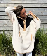 Buzo tipo poncho de polar color crudo con bloque superior en negro y detalles en beige.