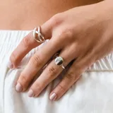 Anillo plateado con diseño de líneas cruzadas y anillo plateado con dije circular.