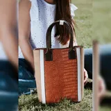 Bolso matero combinado en símil cuero color marrón con textura croco y laterales en color beige. Tiene doble asa de mano color marrón y división interior.
