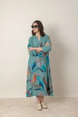 Vestido largo de lino color verde militar con estampado de hojas en tonos azul, naranja y marrón. Tiene cuello mao con botones, mangas tres cuartos y un bolsillo en el pecho.