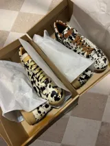 Zapatillas bajas con estampado animal print de vaca en blanco y negro, con cordones marrones y suela color caramelo.