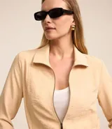 Campera bomber color beige, confeccionada en tejido airflow, con cuello solapa, cierre frontal con cremallera, mangas largas y puños/bajo elásticos.