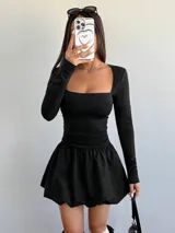 Vestido corto negro con escote cuadrado, mangas largas y falda con volumen.