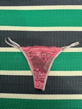 Bombacha tanga color salmón con frente de encaje elastizado y espalda de tul elastizado negro. Tiene elástico lencero color beige y reguladores metálicos a los costados.