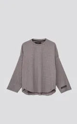 Sweater gris de tejido acanalado, manga larga y cuello redondo. Presenta un corte holgado con bajo redondeado y un pequeño parche negro con logo en la manga izquierda.