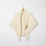 Ruana color crudo de tejido grueso con flecos en el borde inferior y cierre con hebilla de cuero.